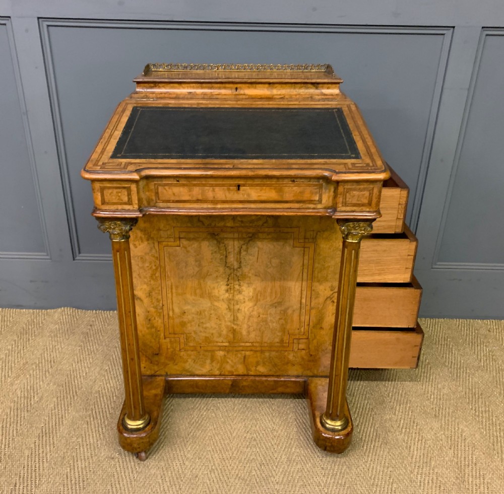 A Victorian burr walnut davenport desk featuring a sloped dark leather inset writing surface, brass gallery rail, side drawers, and fluted column supports. View XVII
