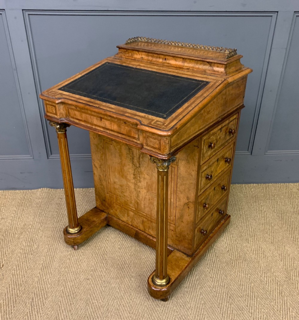 A Victorian burr walnut davenport desk featuring a sloped dark leather inset writing surface, brass gallery rail, side drawers, and fluted column supports. View XX