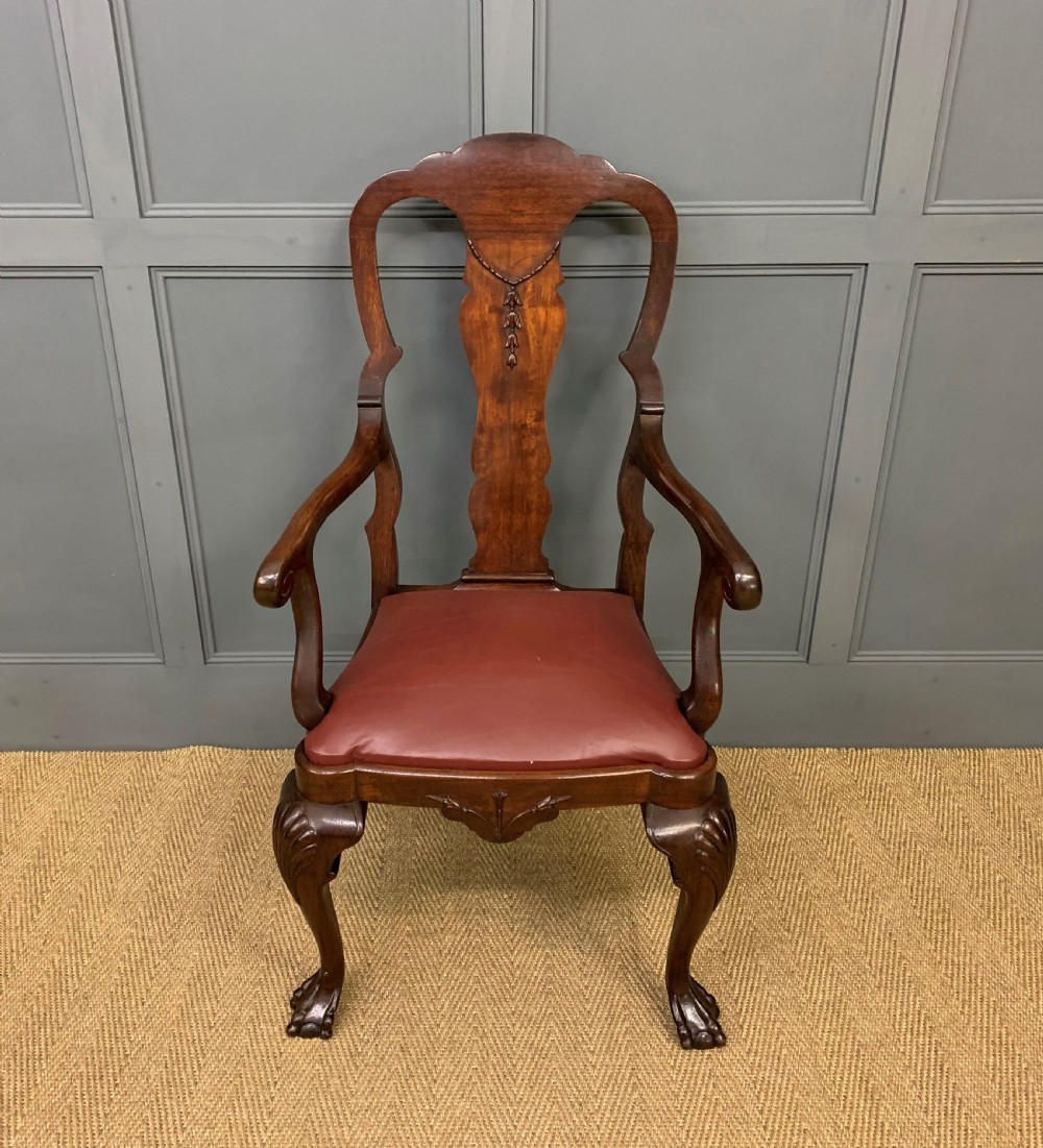 A walnut high-back armchair featuring a carved back splat, reddish-brown leather seat, shaped arms, and carved cabriole legs ending in claw and ball feet.