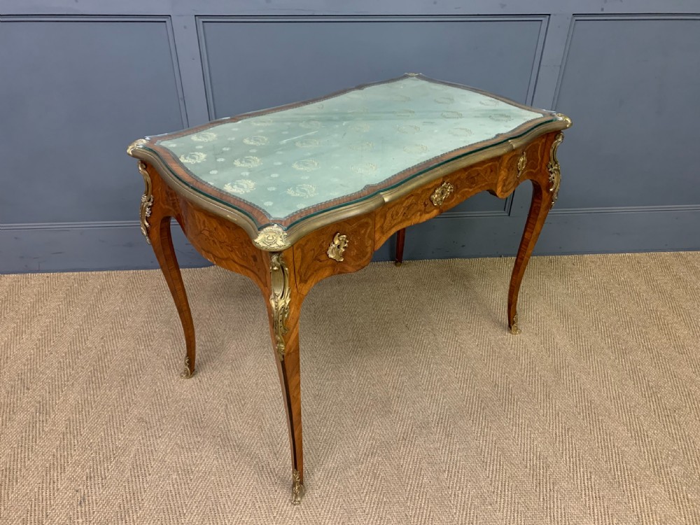 A French Louis XV style bureau plat featuring marquetry floral inlay, gilt-bronze mounts, cabriole legs, and a mint green patterned textile top under protective glass.