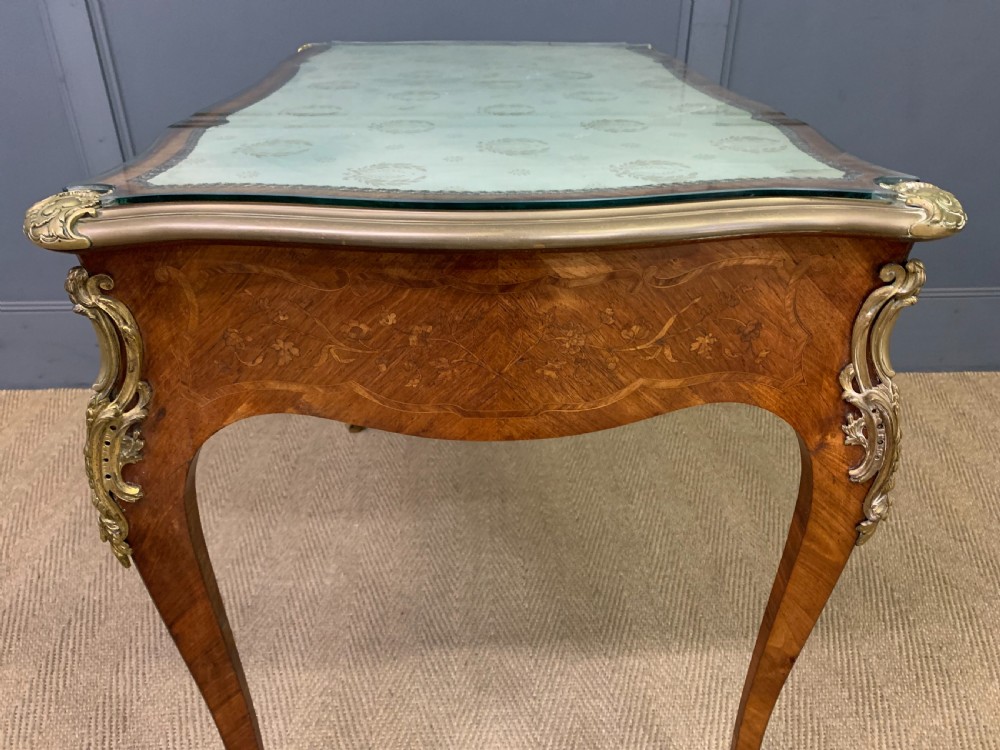 A French Louis XV style bureau plat featuring marquetry floral inlay, gilt-bronze mounts, cabriole legs, and a mint green patterned textile top under protective glass. View XVI
