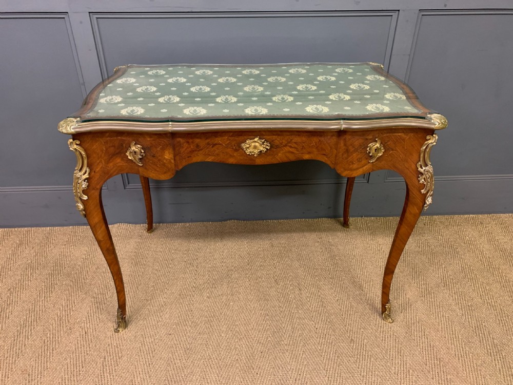 A French Louis XV style bureau plat featuring marquetry floral inlay, gilt-bronze mounts, cabriole legs, and a mint green patterned textile top under protective glass. View XVII