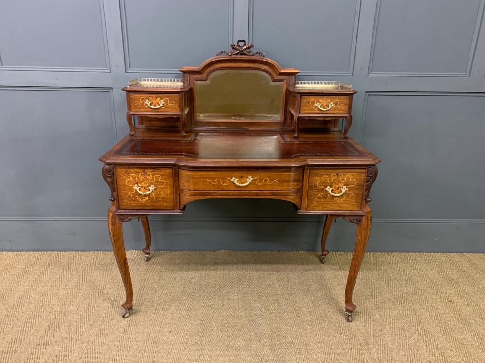 A Victorian mahogany writing desk featuring floral marquetry inlay, a gold-tooled leather insert, a raised superstructure with two drawers and a central mirror, resting on cabriole legs with brass castors. View II
