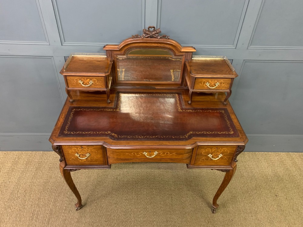 A Victorian mahogany writing desk featuring floral marquetry inlay, a gold-tooled leather insert, a raised superstructure with two drawers and a central mirror, resting on cabriole legs with brass castors. View III