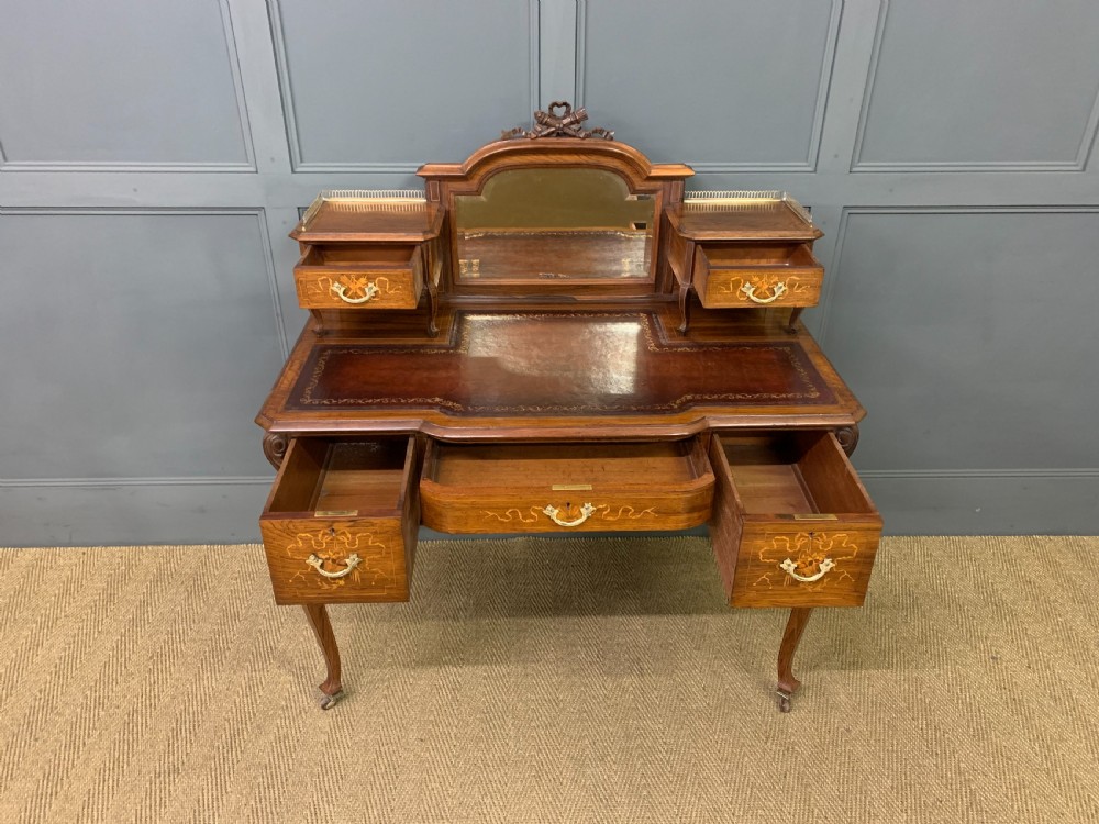 A Victorian mahogany writing desk featuring floral marquetry inlay, a gold-tooled leather insert, a raised superstructure with two drawers and a central mirror, resting on cabriole legs with brass castors. View IV