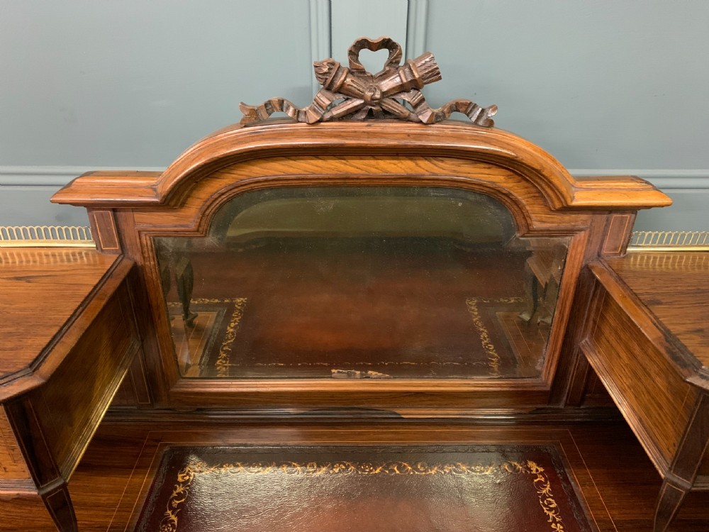 A Victorian mahogany writing desk featuring floral marquetry inlay, a gold-tooled leather insert, a raised superstructure with two drawers and a central mirror, resting on cabriole legs with brass castors. View V