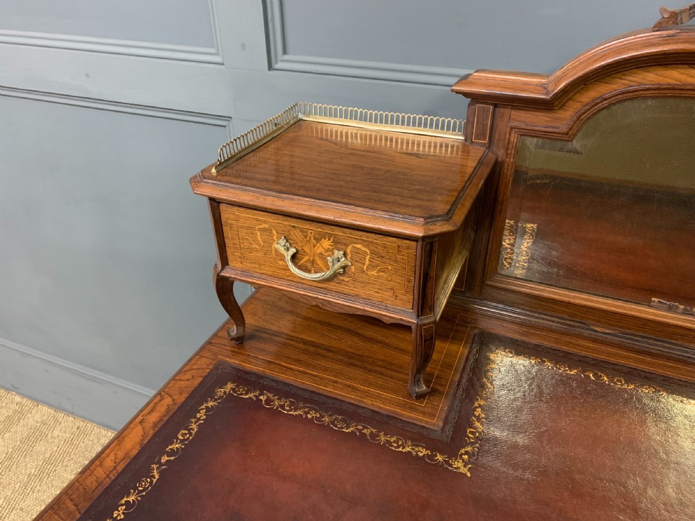 A Victorian mahogany writing desk featuring floral marquetry inlay, a gold-tooled leather insert, a raised superstructure with two drawers and a central mirror, resting on cabriole legs with brass castors. View VII