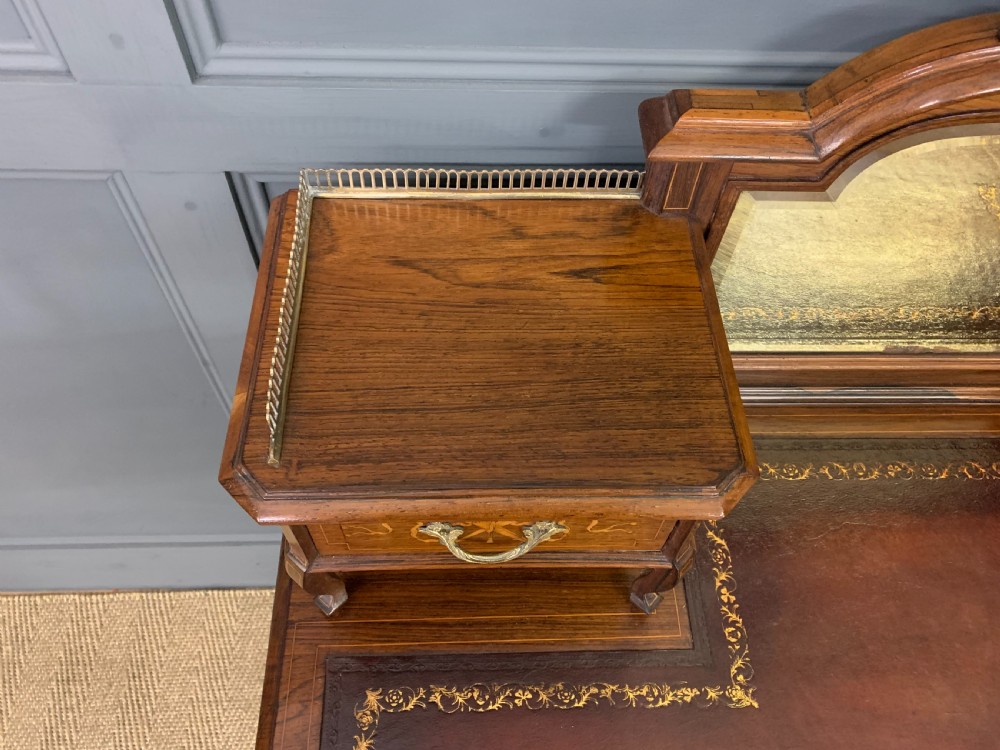 A Victorian mahogany writing desk featuring floral marquetry inlay, a gold-tooled leather insert, a raised superstructure with two drawers and a central mirror, resting on cabriole legs with brass castors. View VIII