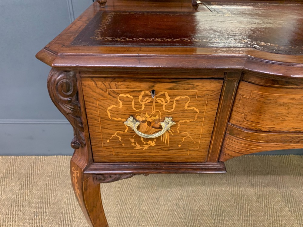A Victorian mahogany writing desk featuring floral marquetry inlay, a gold-tooled leather insert, a raised superstructure with two drawers and a central mirror, resting on cabriole legs with brass castors. View X