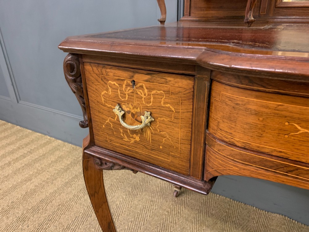 A Victorian mahogany writing desk featuring floral marquetry inlay, a gold-tooled leather insert, a raised superstructure with two drawers and a central mirror, resting on cabriole legs with brass castors. View XI