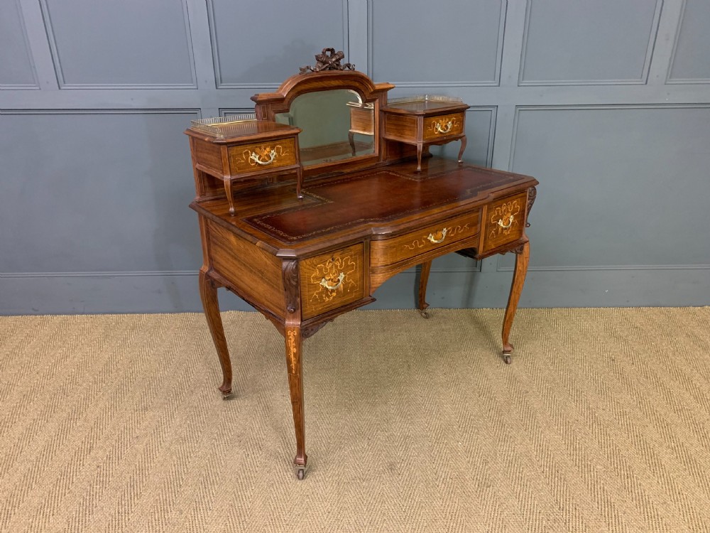 A Victorian mahogany writing desk featuring floral marquetry inlay, a gold-tooled leather insert, a raised superstructure with two drawers and a central mirror, resting on cabriole legs with brass castors. View XIV