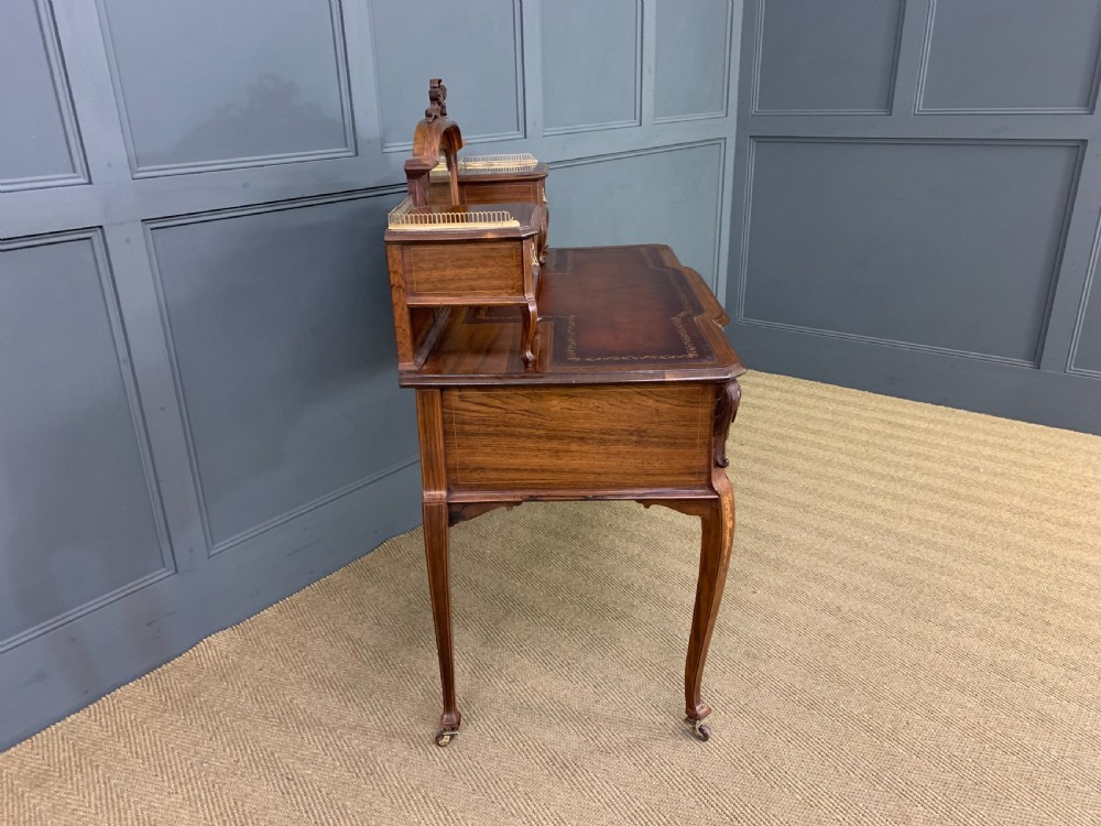 A Victorian mahogany writing desk featuring floral marquetry inlay, a gold-tooled leather insert, a raised superstructure with two drawers and a central mirror, resting on cabriole legs with brass castors. View XVII