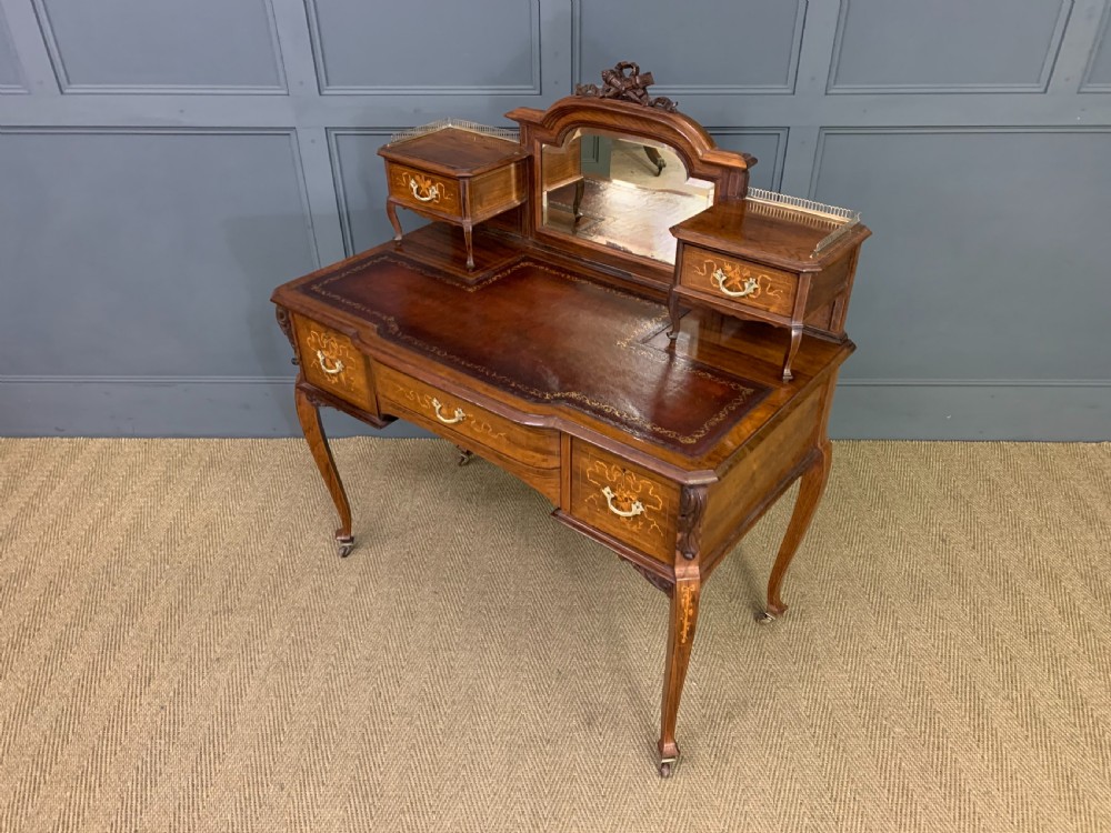 A Victorian mahogany writing desk featuring floral marquetry inlay, a gold-tooled leather insert, a raised superstructure with two drawers and a central mirror, resting on cabriole legs with brass castors. View XIX