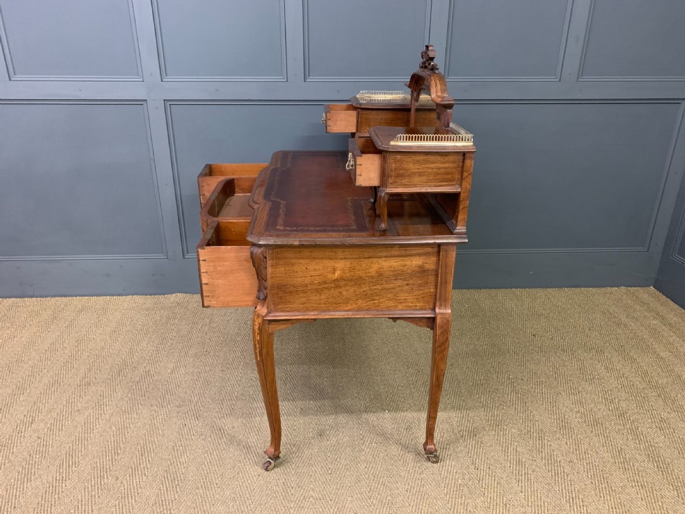 A Victorian mahogany writing desk featuring floral marquetry inlay, a gold-tooled leather insert, a raised superstructure with two drawers and a central mirror, resting on cabriole legs with brass castors. View XX