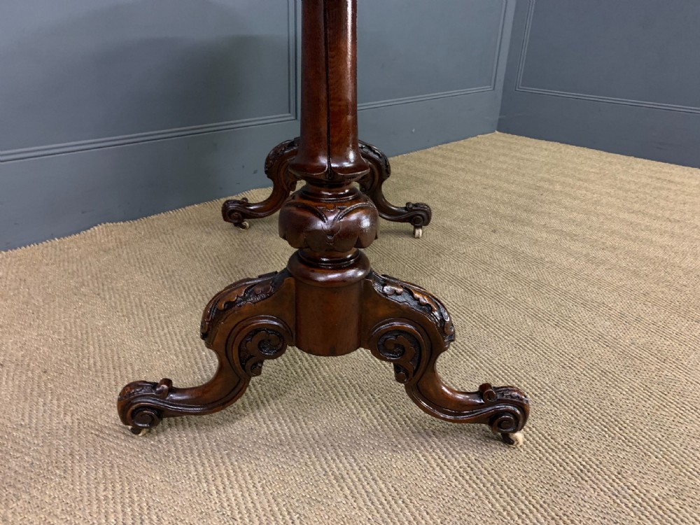An oval Victorian burr walnut stretcher table featuring floral inlay, turned end columns, carved splayed legs, and ceramic castors. View VI