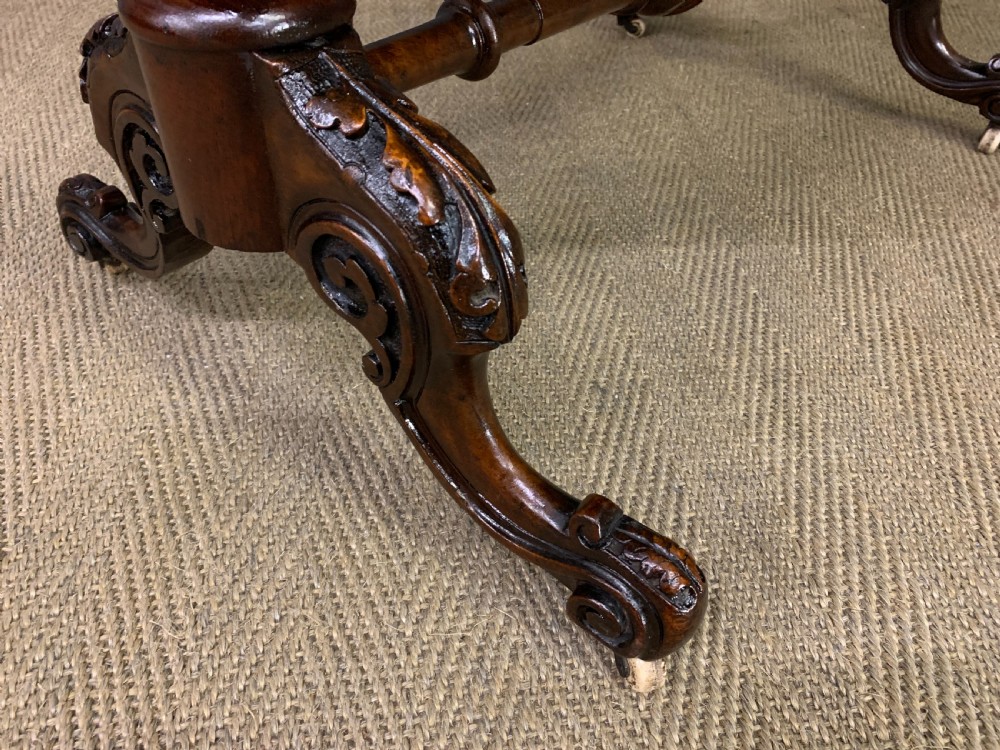 An oval Victorian burr walnut stretcher table featuring floral inlay, turned end columns, carved splayed legs, and ceramic castors. View VIII