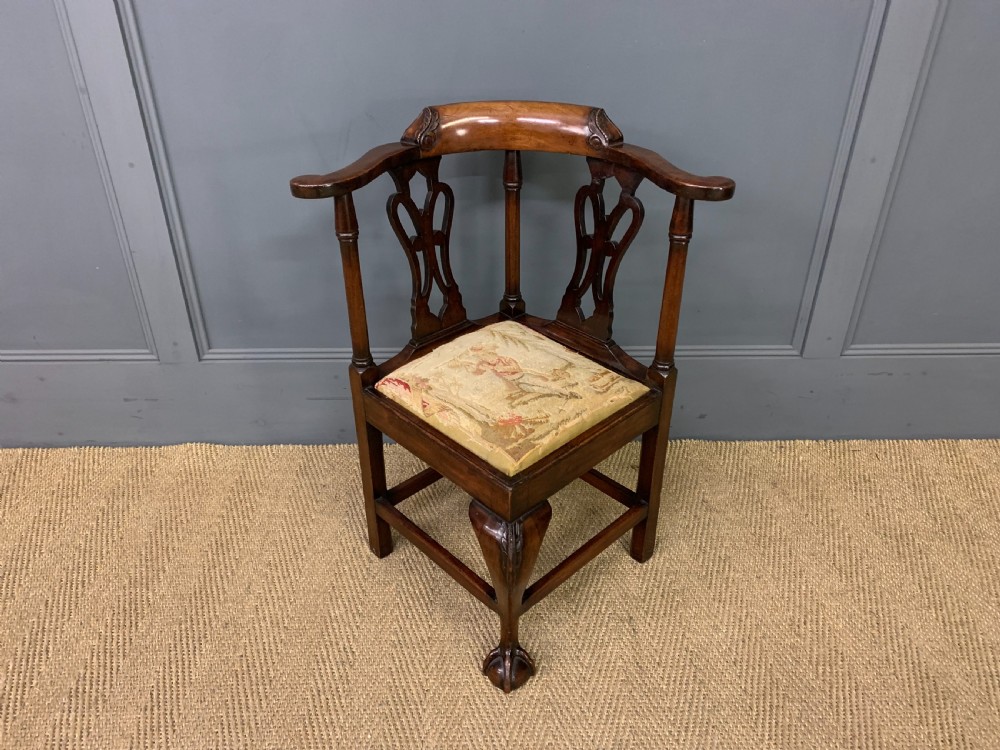 A Georgian style walnut corner chair with a curved crest rail, pierced back splats, a tapestry seat pad, and a central cabriole front leg ending in a claw and ball foot.