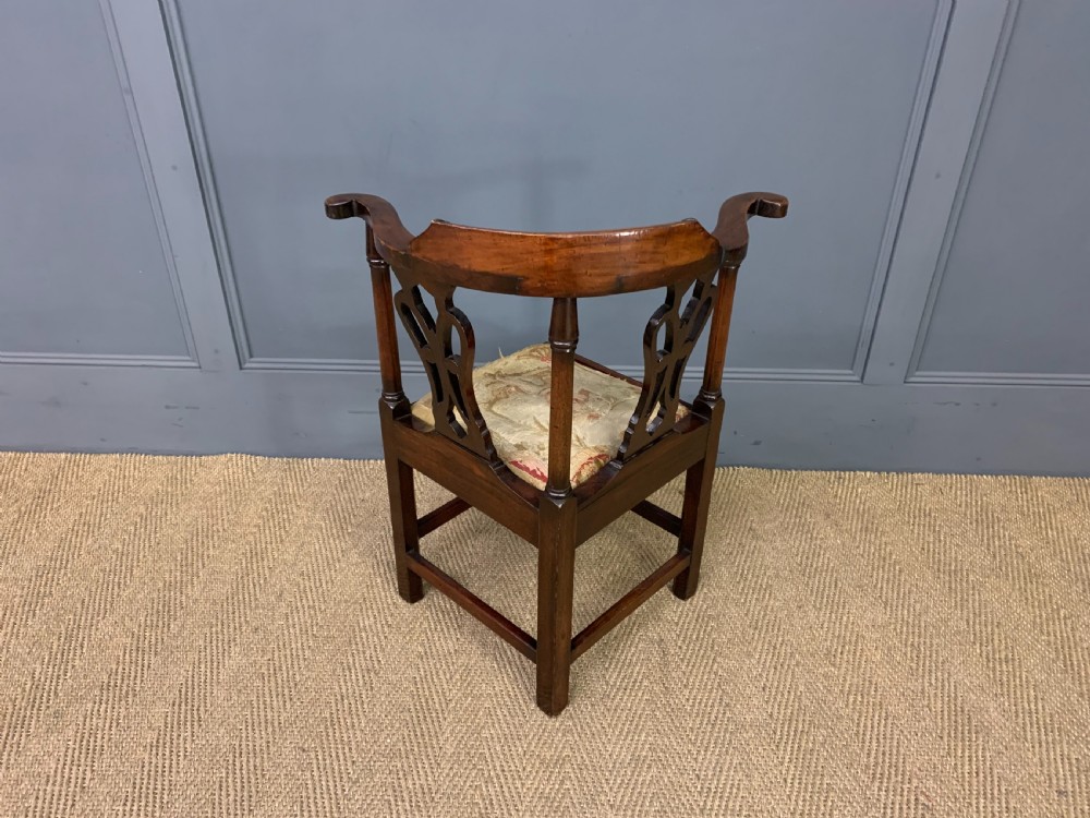 A Georgian style walnut corner chair with a curved crest rail, pierced back splats, a tapestry seat pad, and a central cabriole front leg ending in a claw and ball foot. View X