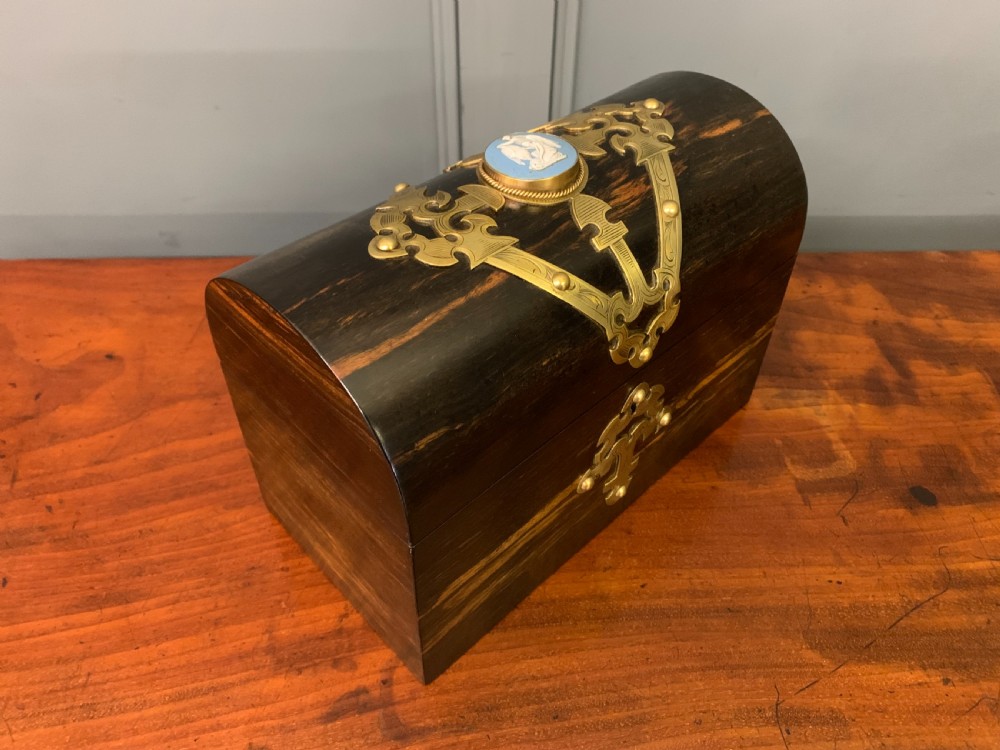A Victorian dome-topped stationery casket crafted from dark variegated coromandel wood, decorated with pierced brass strapwork and a blue and white ceramic cameo inset.