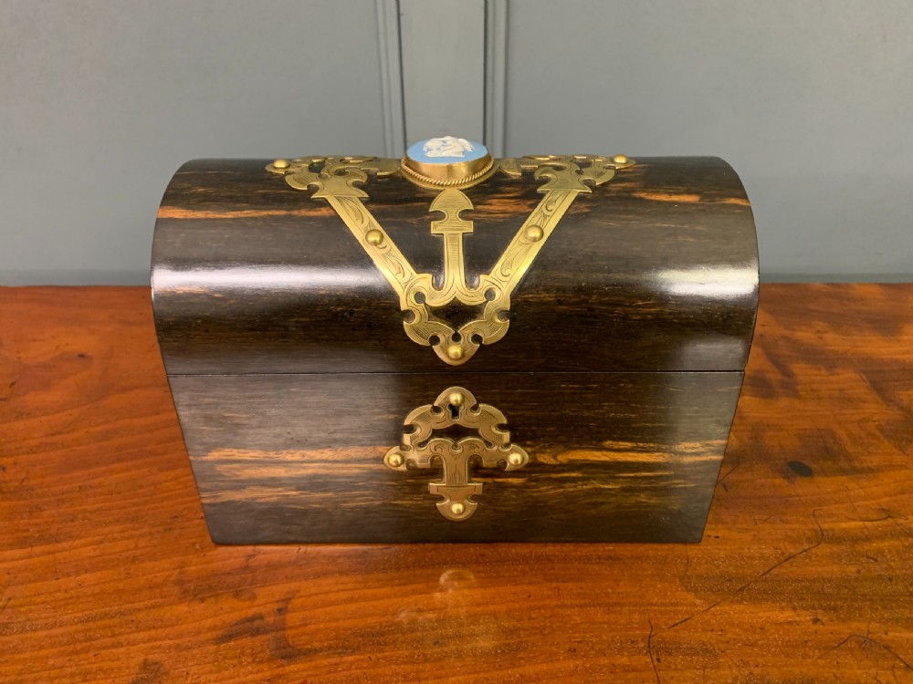 A Victorian dome-topped stationery casket crafted from dark variegated coromandel wood, decorated with pierced brass strapwork and a blue and white ceramic cameo inset. View II