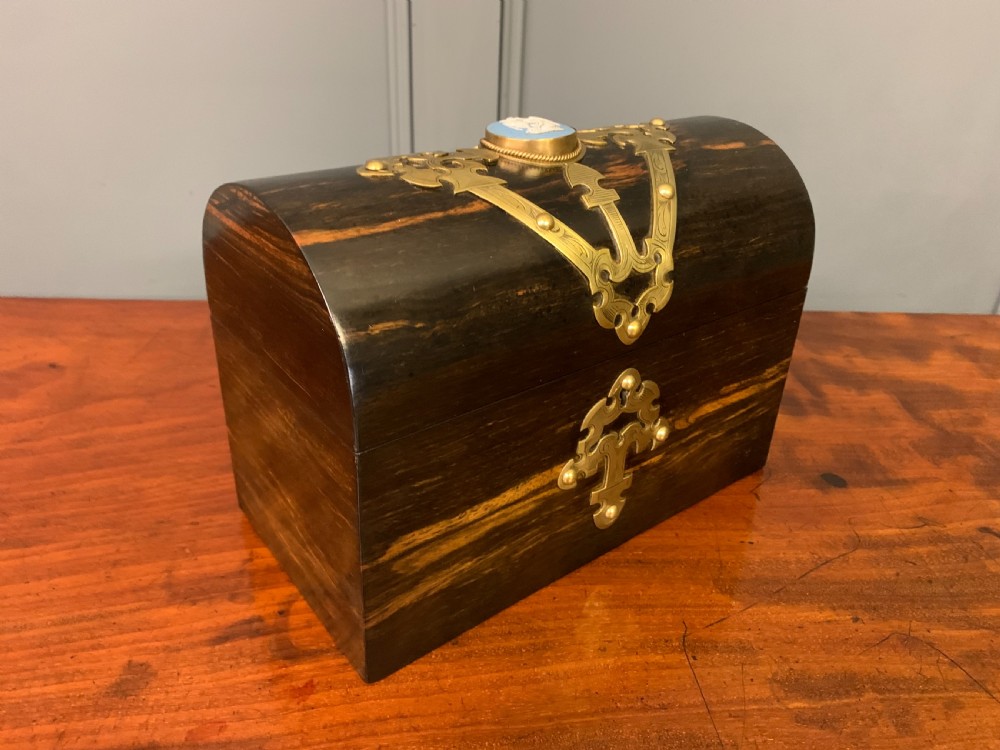 A Victorian dome-topped stationery casket crafted from dark variegated coromandel wood, decorated with pierced brass strapwork and a blue and white ceramic cameo inset. View VI