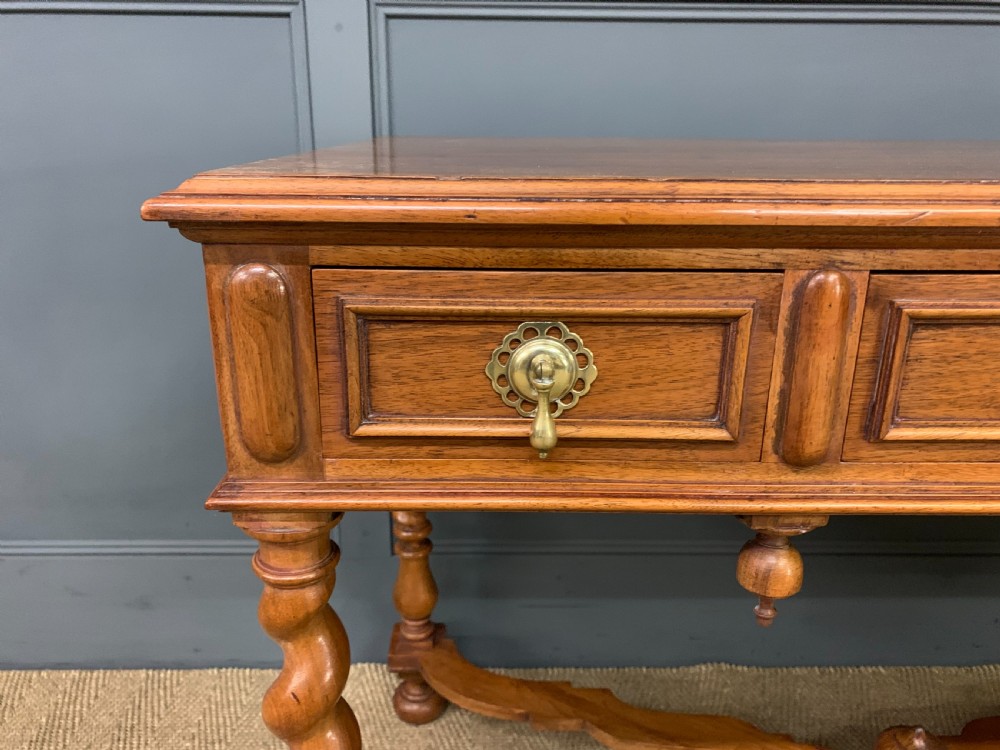 A rectangular walnut side table featuring three drawers with brass teardrop drop-handles, spiral barley twist legs, and a serpentine X-stretcher with a central turned finial. View V