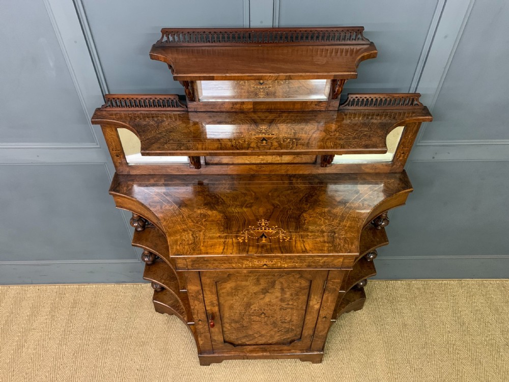 A Victorian burr walnut chiffonier featuring a central cabinet door with floral marquetry, open side tiers with turned spindles, and an upper structure with mirror panels and gallery railings. View V