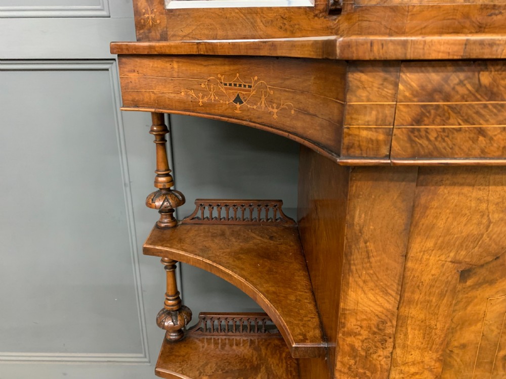 A Victorian burr walnut chiffonier featuring a central cabinet door with floral marquetry, open side tiers with turned spindles, and an upper structure with mirror panels and gallery railings. View X