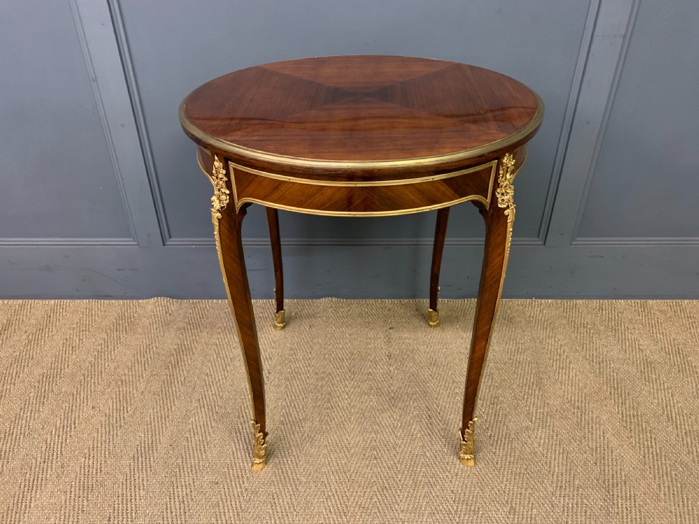 A circular French Louis XV revival centre table featuring quartered rosewood veneers, brass moulding rim, and gilt-bronze mounts on cabriole legs.