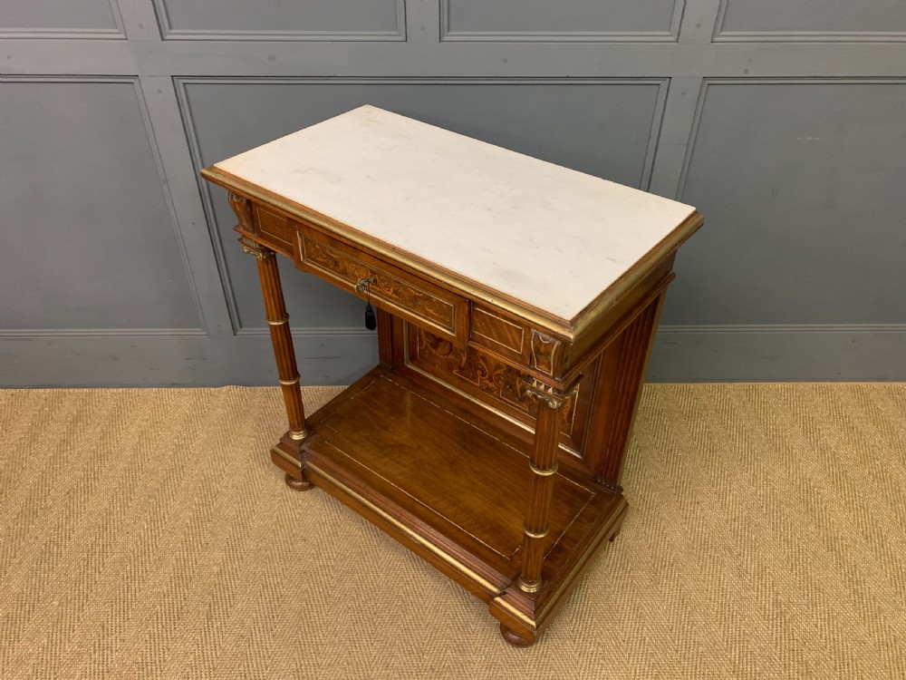 A 19th-century walnut pier table featuring a white marble top, inlaid floral and urn marquetry, fluted front columns with gilt mounts, and a lower open shelf. View XVIII