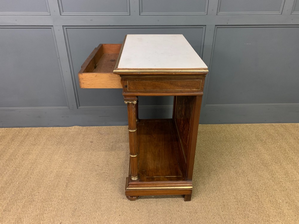 A 19th-century walnut pier table featuring a white marble top, inlaid floral and urn marquetry, fluted front columns with gilt mounts, and a lower open shelf. View XIX