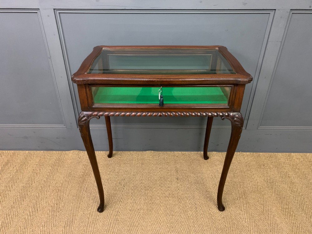 A mahogany bijouterie table featuring a glazed glass top and sides, green fabric interior lining, cabriole legs, and carved shell details on the knees. View II