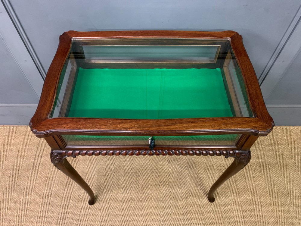 A mahogany bijouterie table featuring a glazed glass top and sides, green fabric interior lining, cabriole legs, and carved shell details on the knees. View IV
