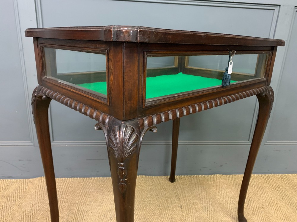 A mahogany bijouterie table featuring a glazed glass top and sides, green fabric interior lining, cabriole legs, and carved shell details on the knees. View VI