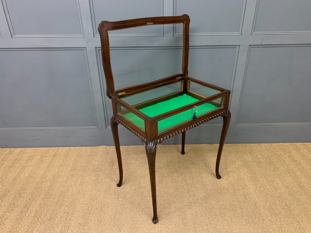 A mahogany bijouterie table featuring a glazed glass top and sides, green fabric interior lining, cabriole legs, and carved shell details on the knees. View IX