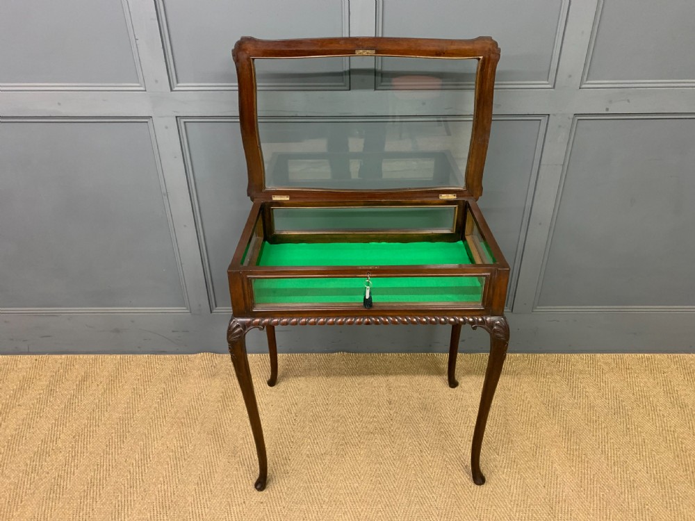 A mahogany bijouterie table featuring a glazed glass top and sides, green fabric interior lining, cabriole legs, and carved shell details on the knees. View X