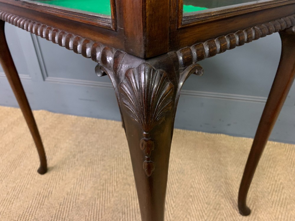 A mahogany bijouterie table featuring a glazed glass top and sides, green fabric interior lining, cabriole legs, and carved shell details on the knees. View XII