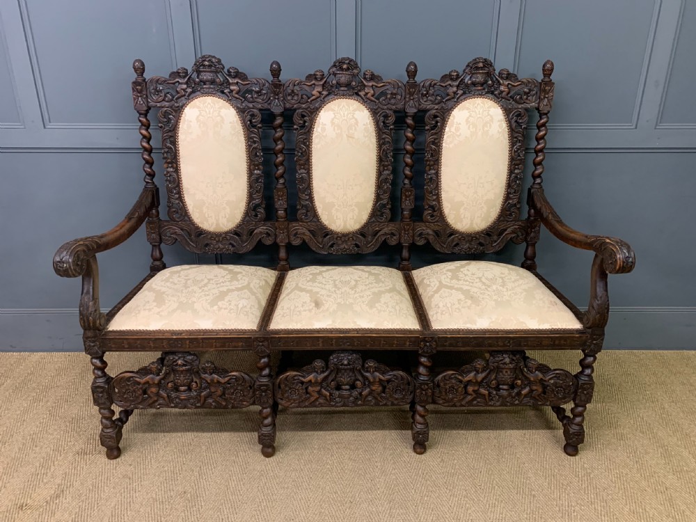 A 19th-century Carolean style walnut three-seat settee featuring barley twist columns, ornate openwork cherub carvings, and cream damask upholstered back panels and seats.