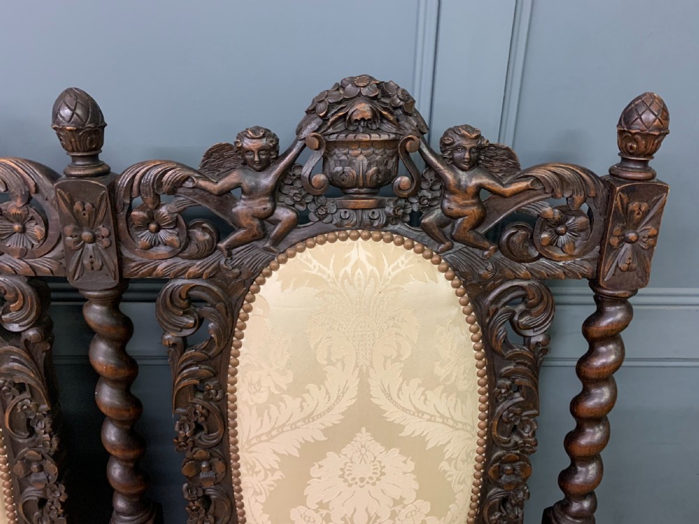 A 19th-century Carolean style walnut three-seat settee featuring barley twist columns, ornate openwork cherub carvings, and cream damask upholstered back panels and seats. View IV