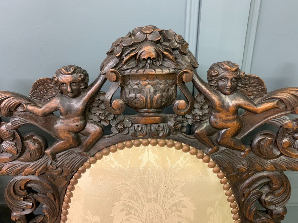 A 19th-century Carolean style walnut three-seat settee featuring barley twist columns, ornate openwork cherub carvings, and cream damask upholstered back panels and seats. View V