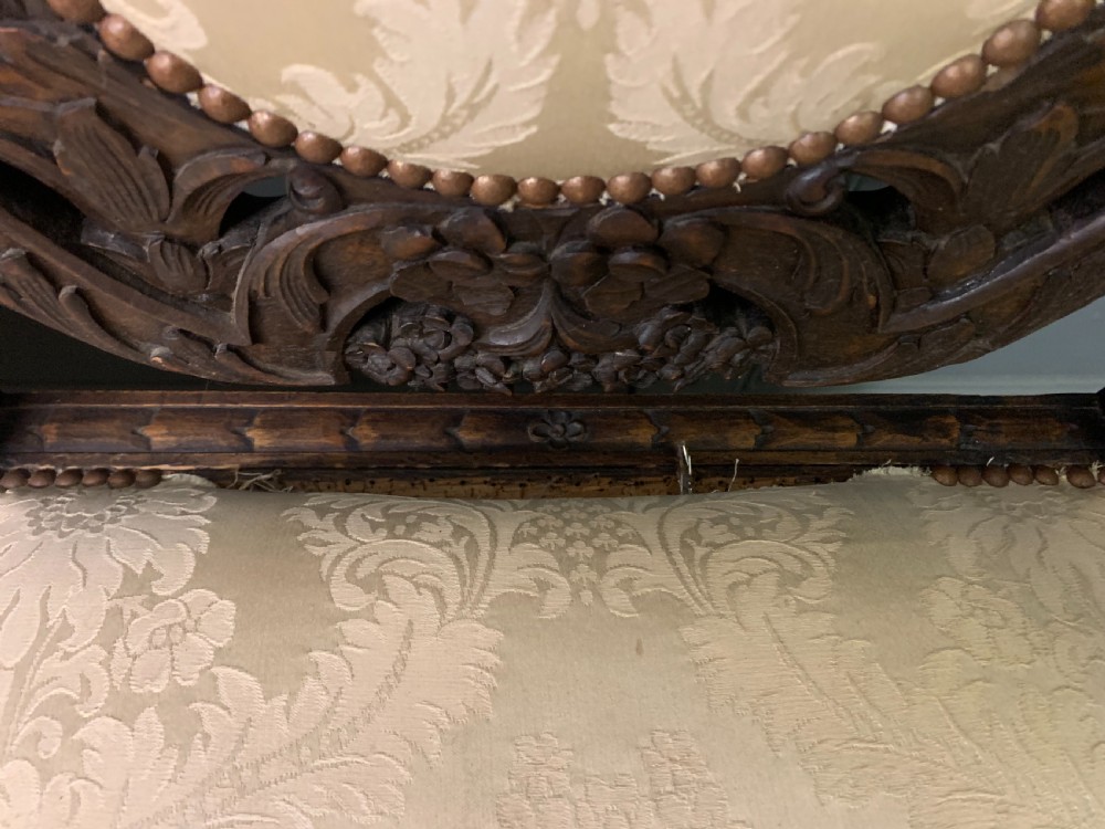 A 19th-century Carolean style walnut three-seat settee featuring barley twist columns, ornate openwork cherub carvings, and cream damask upholstered back panels and seats. View VIII