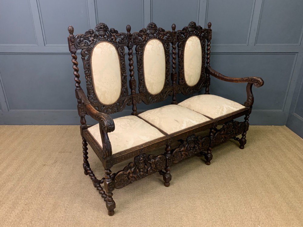 A 19th-century Carolean style walnut three-seat settee featuring barley twist columns, ornate openwork cherub carvings, and cream damask upholstered back panels and seats. View IX