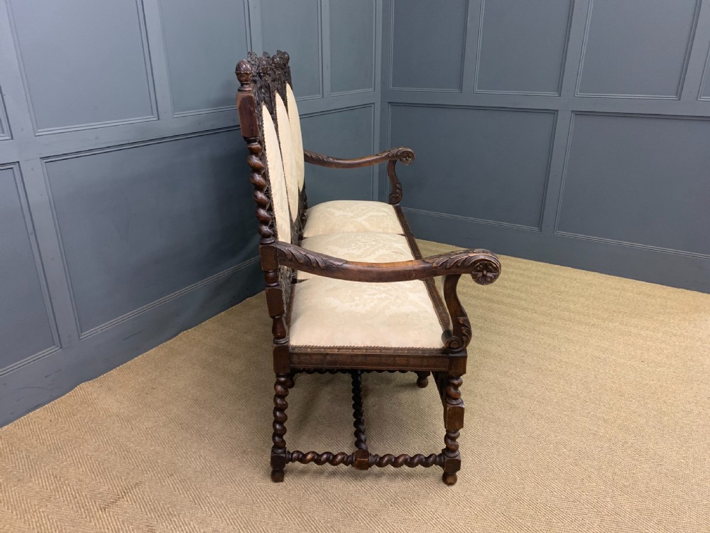 A 19th-century Carolean style walnut three-seat settee featuring barley twist columns, ornate openwork cherub carvings, and cream damask upholstered back panels and seats. View X