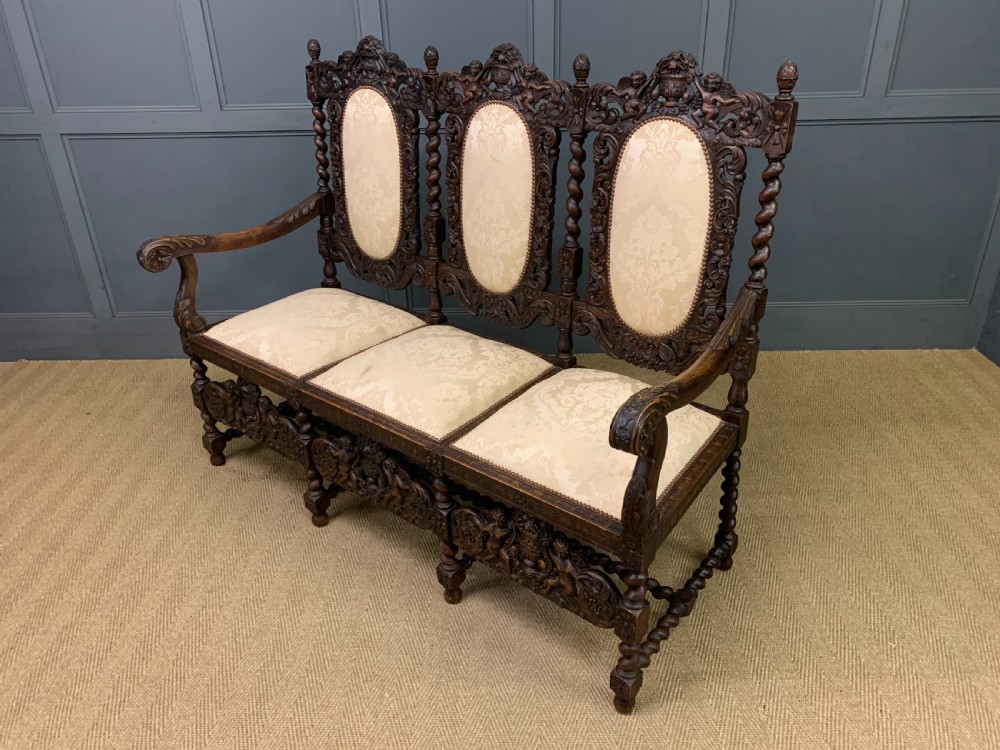 A 19th-century Carolean style walnut three-seat settee featuring barley twist columns, ornate openwork cherub carvings, and cream damask upholstered back panels and seats. View XI