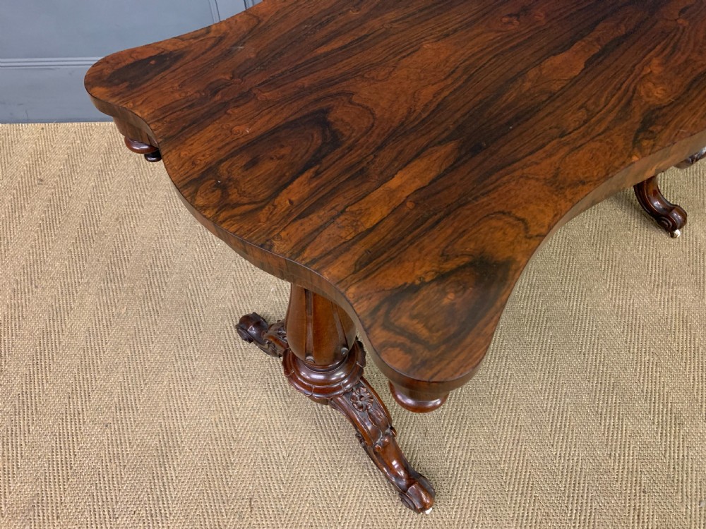 Victorian rosewood stretcher table featuring a serpentine top with figured grain, turned end supports, a carved central stretcher, and ceramic castors. View XI