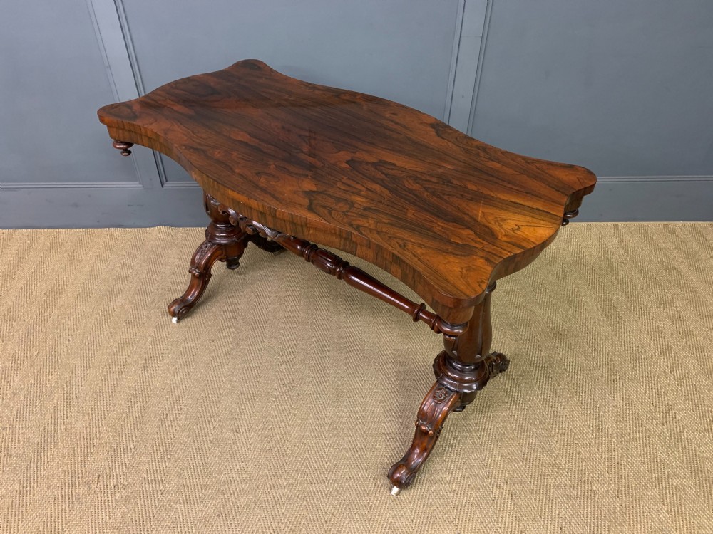 Victorian rosewood stretcher table featuring a serpentine top with figured grain, turned end supports, a carved central stretcher, and ceramic castors. View XII