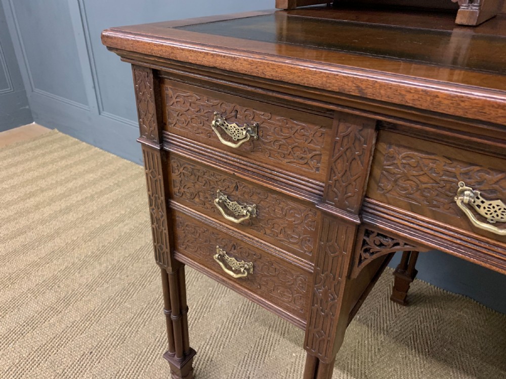 Victorian mahogany writing desk featuring a gallery superstructure with pierced fretwork, a brown leather inset surface, and multiple drawers with brass drop handles. View VI