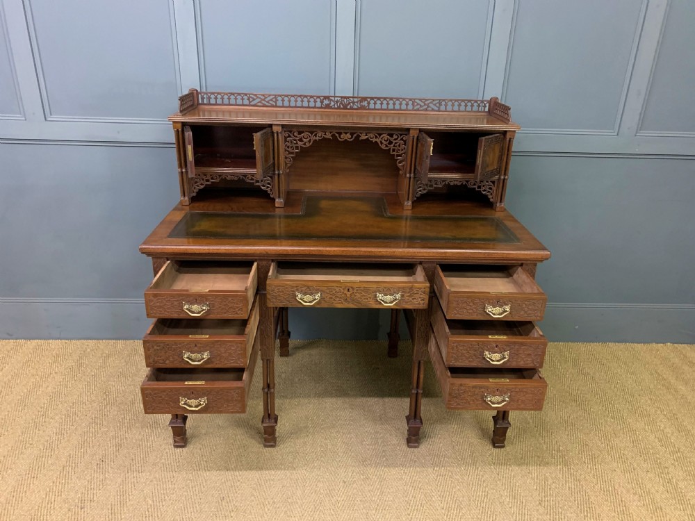 Victorian mahogany writing desk featuring a gallery superstructure with pierced fretwork, a brown leather inset surface, and multiple drawers with brass drop handles. View XV