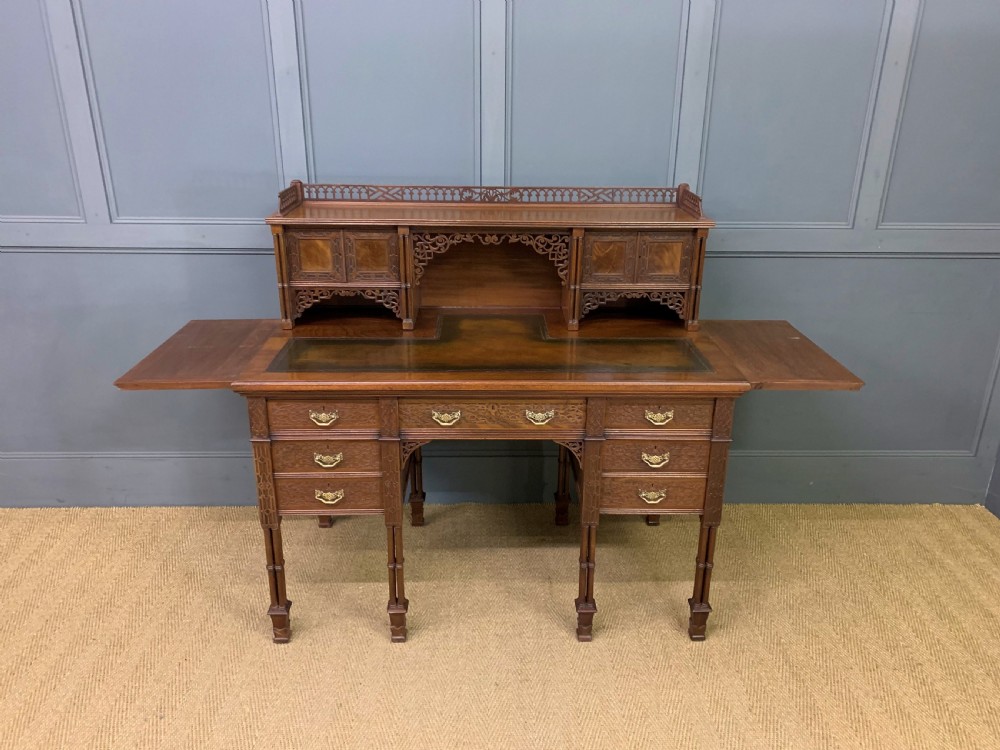 Victorian mahogany writing desk featuring a gallery superstructure with pierced fretwork, a brown leather inset surface, and multiple drawers with brass drop handles. View XVII
