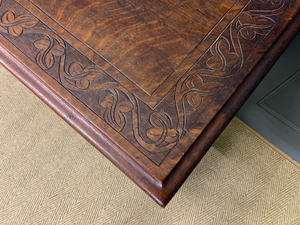 A dark carved oak side table featuring intricate lunette carvings, brass drop handles, three drawers, turned legs, and a stretcher base. View VII